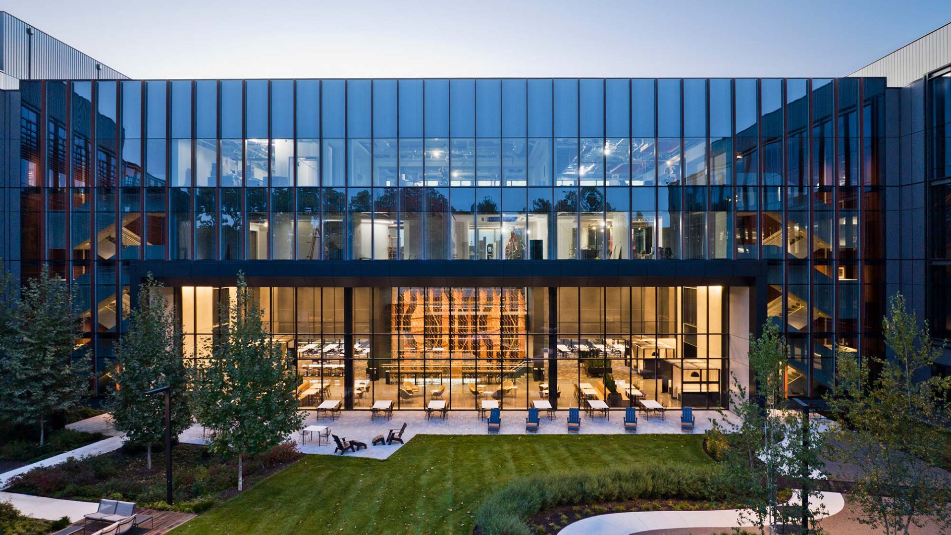 A building with glass windows and people sitting on the grass.