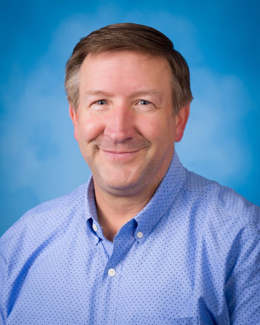 A man in blue shirt smiling for the camera.