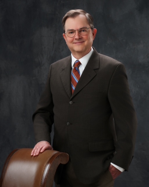 A man in suit and tie holding a chair.